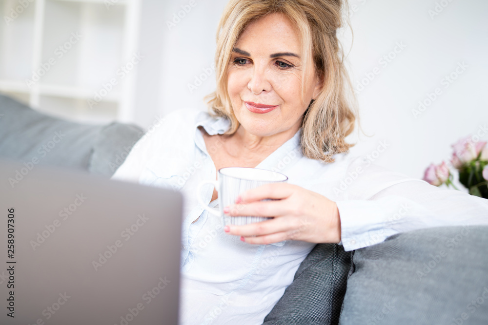 Best Age Frau sitzt mit einer Tasse Kaffee auf der Couch und schaut in ihren Laptop Best Age Frau sitzt mit einer Tasse Kaffee auf der Couch und schaut in ihren Laptop