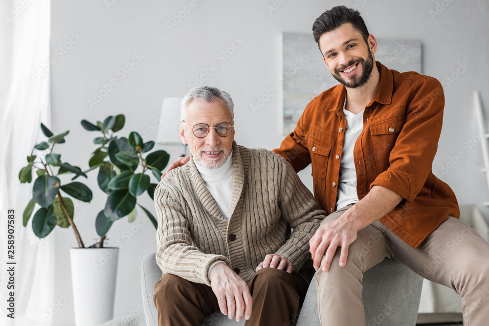 happy senior father in glasses sitting near handsome and cheerful son at home happy senior father in glasses sitting near handsome and cheerful son at home