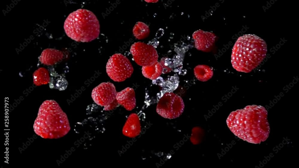 Ripe raspberry with water fly and rotates in the air on a black background