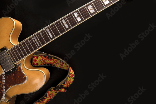 Vintage archtop guitar in natural maple close-up with colored strap from above on black background