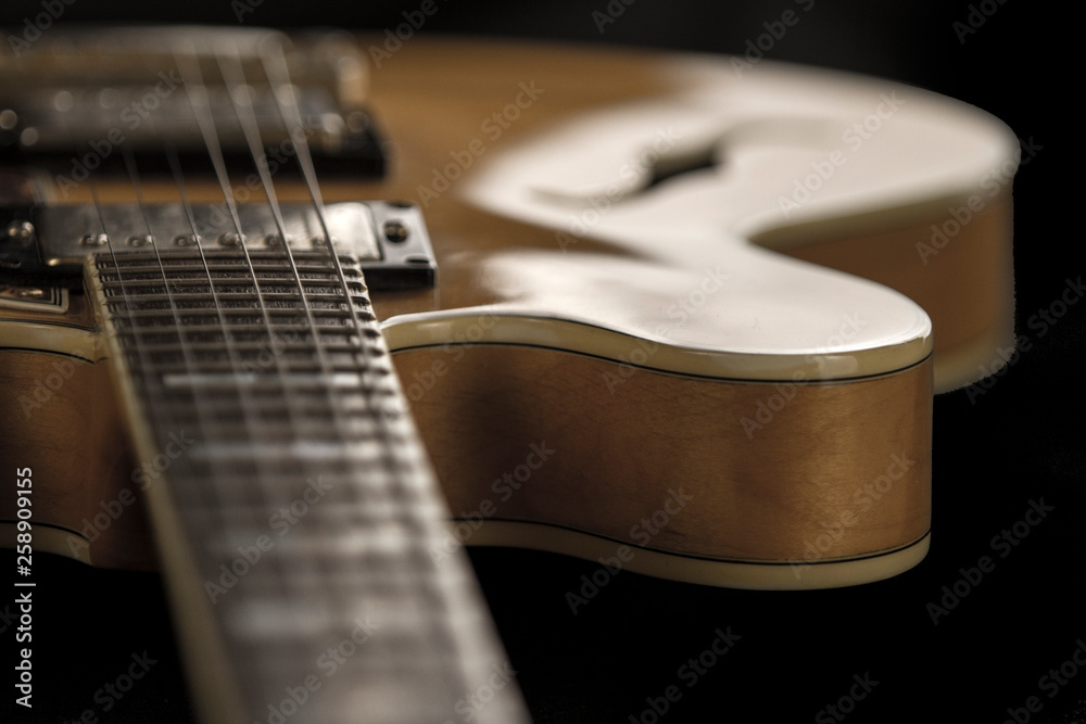 Fototapeta premium Vintage archtop guitar in natural maple close-up high angle view on black background, frets and veins of maple wood detail in selective focus