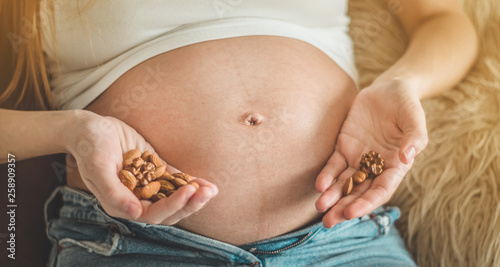 Happy pregnant woman at home eating fresh nuts - almonds, walnuts. Healthy pregnancy concept