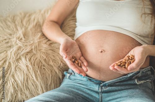 Happy pregnant woman at home eating fresh nuts - almonds, walnuts. Healthy pregnancy concept