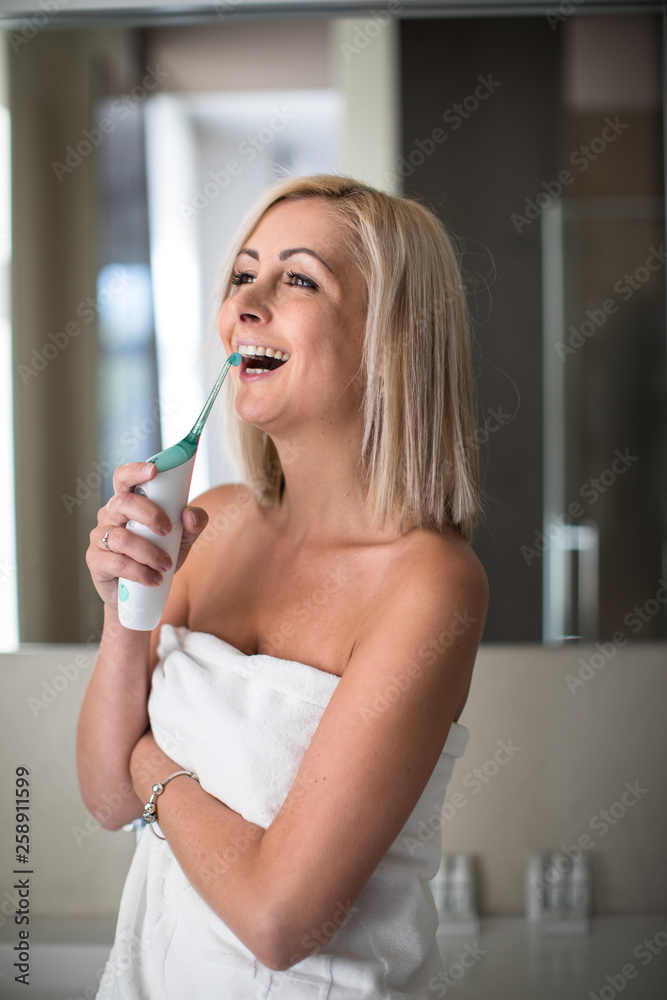 Pretty, middle aged woman brushing her teeth in a modern design bathroom - using the tooth shower instead of dental floss and looking very happy about not having to floss anylonger Pretty, middle aged woman brushing her teeth in a modern design bathroom - using the tooth shower instead of dental floss and looking very happy about not having to floss anylonger