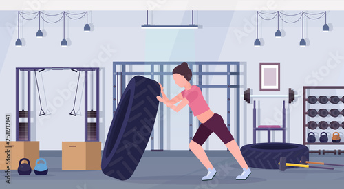 sports woman flipping a tire doing hard exercises girl working out in gym crossfit training healthy lifestyle concept modern health club studio interior horizontal