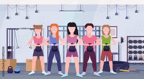 sports people group doing exercises with kettlebell girls with guy training in gym workout healthy lifestyle concept modern health club studio interior horizontal
