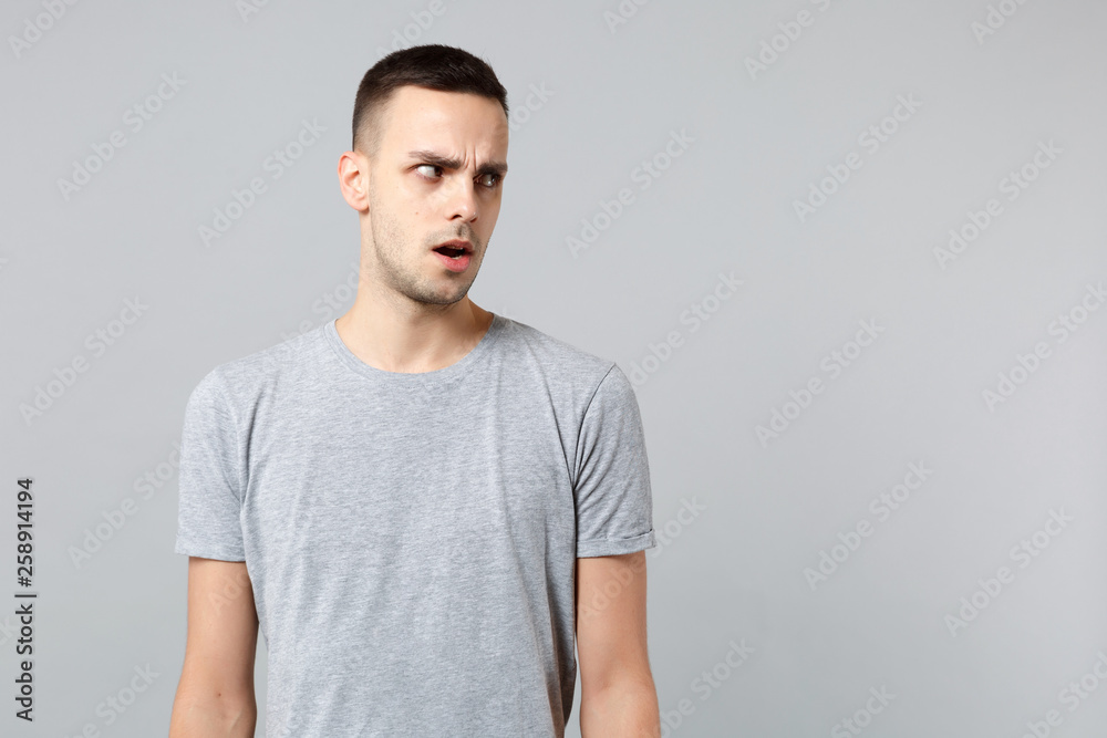Portrait of perplexed puzzled young man in casual clothes standing and looking aside isolated on grey wall background. People sincere emotions, lifestyle concept. Mock up copy space. Advertising area. Portrait of perplexed puzzled young man in casual clothes standing and looking aside isolated on grey wall background. People sincere emotions, lifestyle concept. Mock up copy space. Advertising area.
