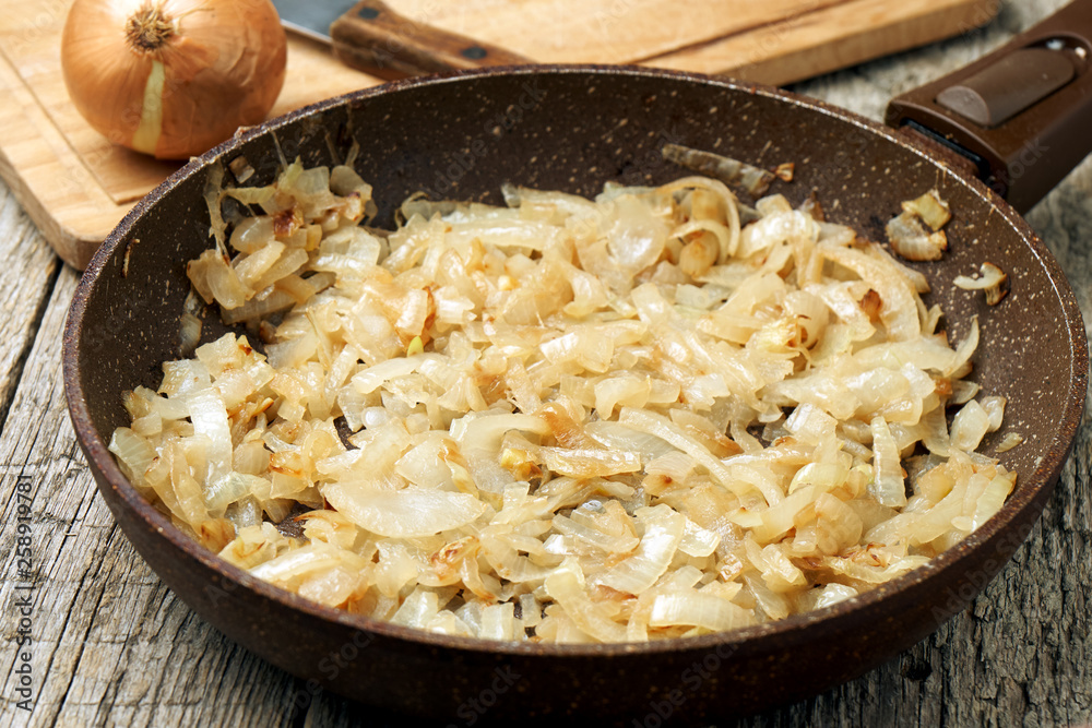 Stone coated frying pan with freshly fried onion on the wooden table Stone coated frying pan with freshly fried onion on the wooden table