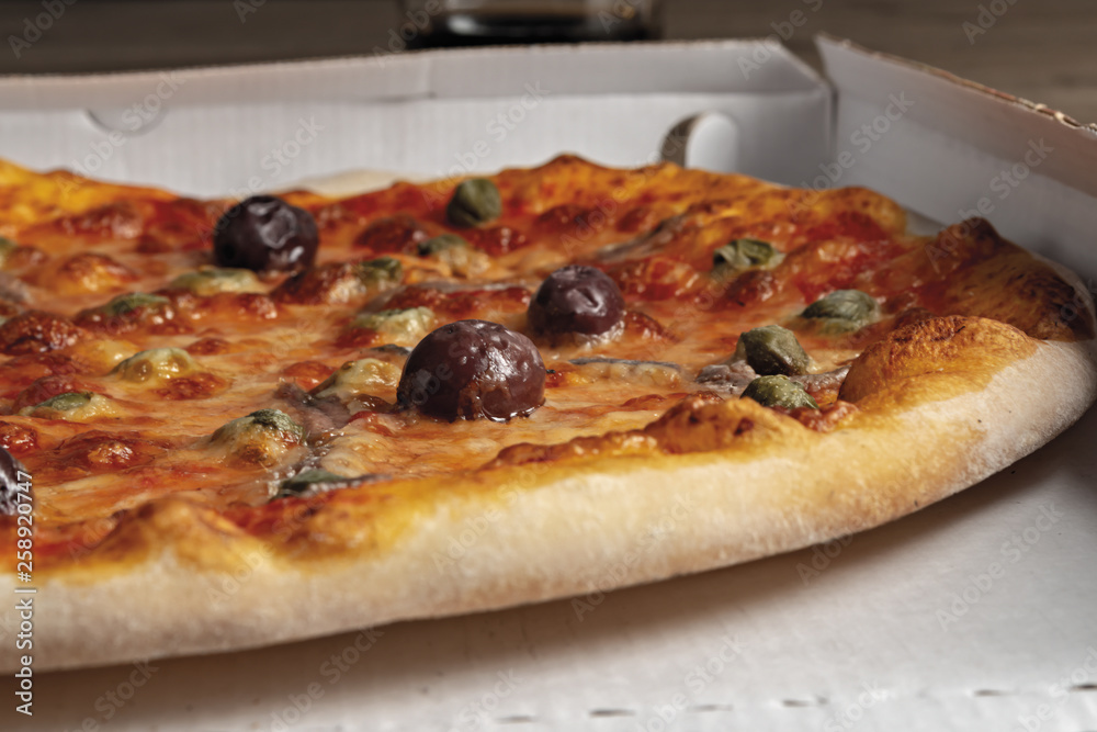 pizza pomodoro acciughe capperi olive nere intera nella scatola dal basso primo piano vista destra pizza pomodoro acciughe capperi olive nere intera nella scatola dal basso primo piano vista destra