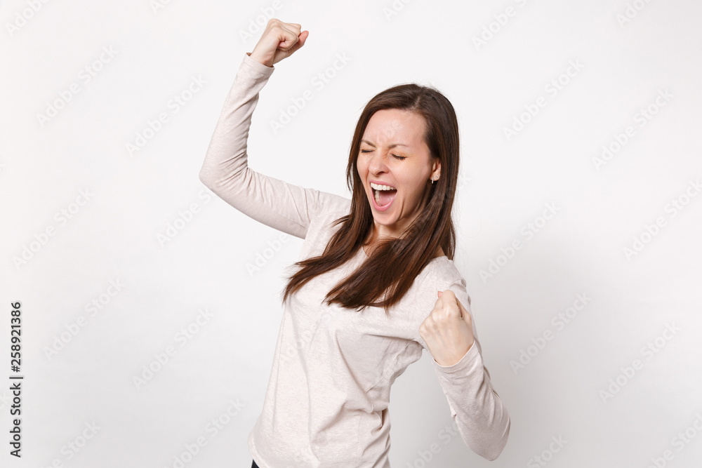 Portrait of happy young woman in light clothes keeping eyes closed, clenching fists like winner isolated on white background in studio. People sincere emotions, lifestyle concept. Mock up copy space. Portrait of happy young woman in light clothes keeping eyes closed, clenching fists like winner isolated on white background in studio. People sincere emotions, lifestyle concept. Mock up copy space.