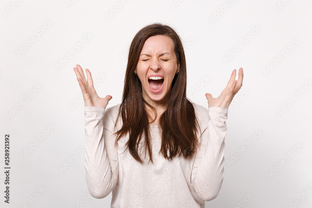 Portrait of crazy screaming young woman in light clothes keeping eyes closed spreading hands isolated on white wall background in studio. People sincere emotions lifestyle concept. Mock up copy space. Portrait of crazy screaming young woman in light clothes keeping eyes closed spreading hands isolated on white wall background in studio. People sincere emotions lifestyle concept. Mock up copy space.