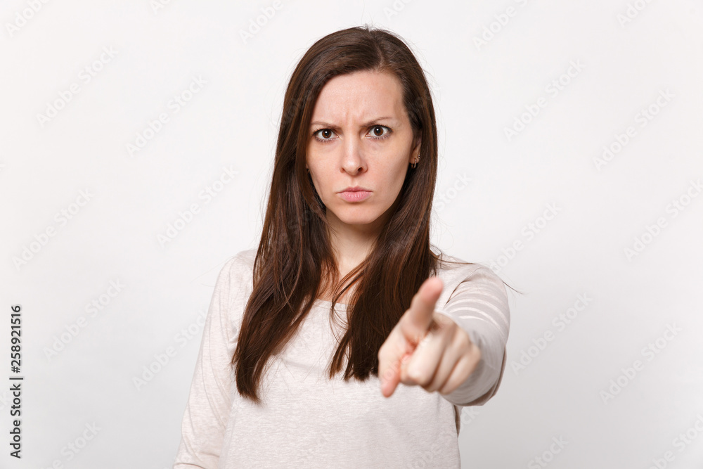 Portrait of concerned strict young woman in light clothes pointing index finger on camera isolated on white wall background in studio. People sincere emotions, lifestyle concept. Mock up copy space. Portrait of concerned strict young woman in light clothes pointing index finger on camera isolated on white wall background in studio. People sincere emotions, lifestyle concept. Mock up copy space.