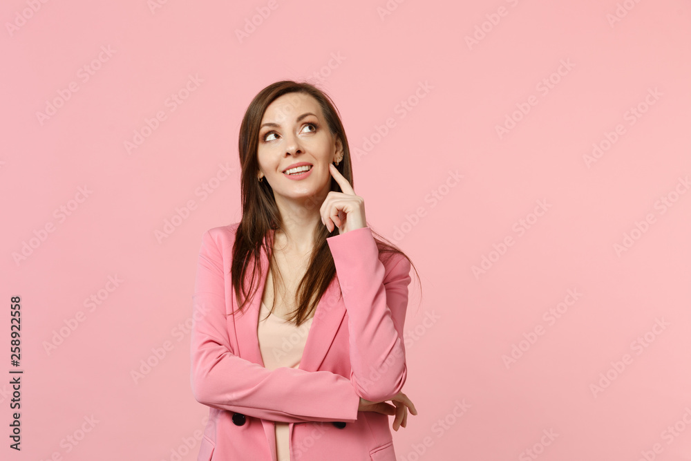 Portrait of dreamful pretty young woman in jacket looking up put hand prop up on chin isolated on pastel pink wall background in studio. People sincere emotions, lifestyle concept. Mock up copy space. Portrait of dreamful pretty young woman in jacket looking up put hand prop up on chin isolated on pastel pink wall background in studio. People sincere emotions, lifestyle concept. Mock up copy space.