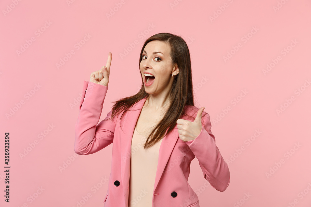 Cheerful young woman keeping mouth open, holding index finger up with new idea, showing thumb up isolated on pastel pink wall background. People sincere emotions lifestyle concept. Mock up copy space. Cheerful young woman keeping mouth open, holding index finger up with new idea, showing thumb up isolated on pastel pink wall background. People sincere emotions lifestyle concept. Mock up copy space.