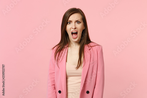 Portrait of shocked angry young woman wearing jacket looking camera screaming and swearing isolated on pastel pink background in studio. People sincere emotions, lifestyle concept. Mock up copy space. © ViDi Studio
