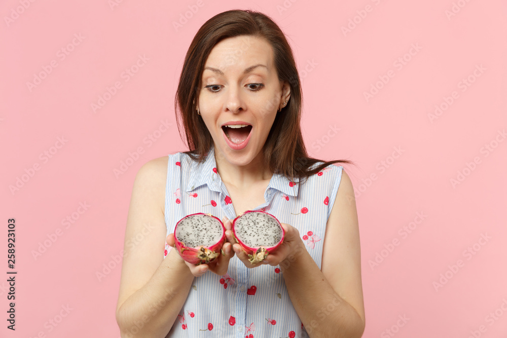Amazed young woman keeping mouth open, holding halfs of fresh ripe pitahaya, dragon fruit isolated on pink pastel wall background. People vivid lifestyle relax vacation concept. Mock up copy space. Amazed young woman keeping mouth open, holding halfs of fresh ripe pitahaya, dragon fruit isolated on pink pastel wall background. People vivid lifestyle relax vacation concept. Mock up copy space.