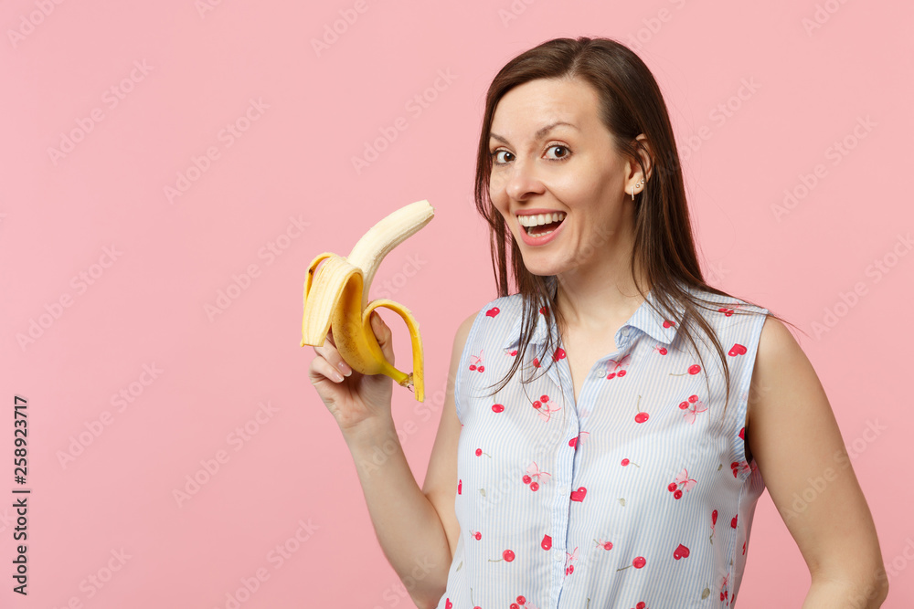 Cheerful young woman in summer clothes hold in hand fresh ripe banana fruit isolated on pink pastel wall background, studio portrait. People vivid lifestyle relax vacation concept. Mock up copy space. Cheerful young woman in summer clothes hold in hand fresh ripe banana fruit isolated on pink pastel wall background, studio portrait. People vivid lifestyle relax vacation concept. Mock up copy space.
