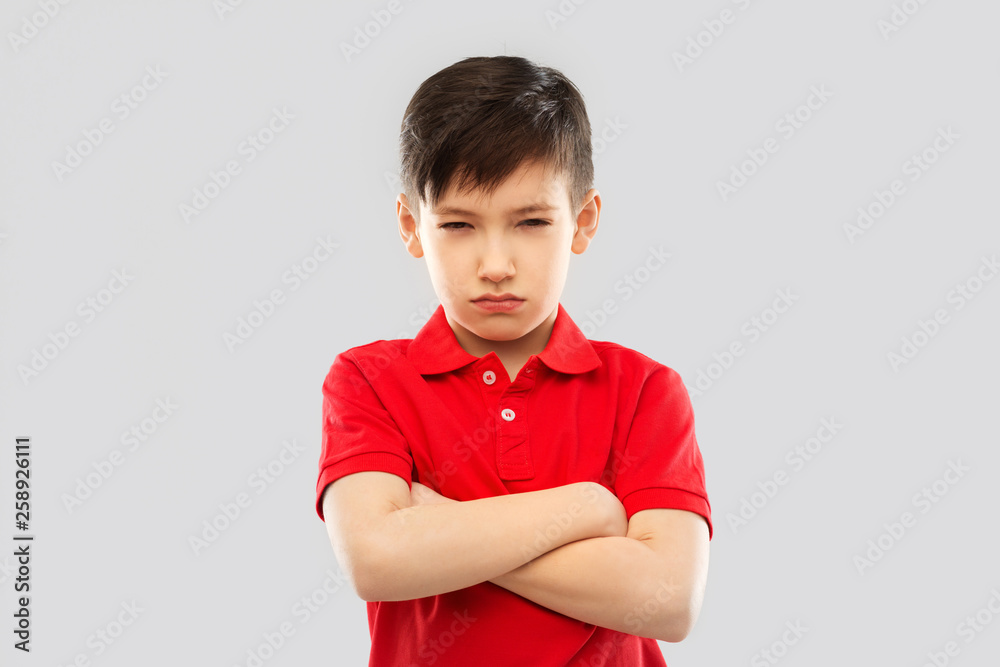 childhood, expressions and people concept - displeased little boy with crossed arms in red polo t-shirt pouting and squinting over grey background childhood, expressions and people concept - displeased little boy with crossed arms in red polo t-shirt pouting and squinting over grey background