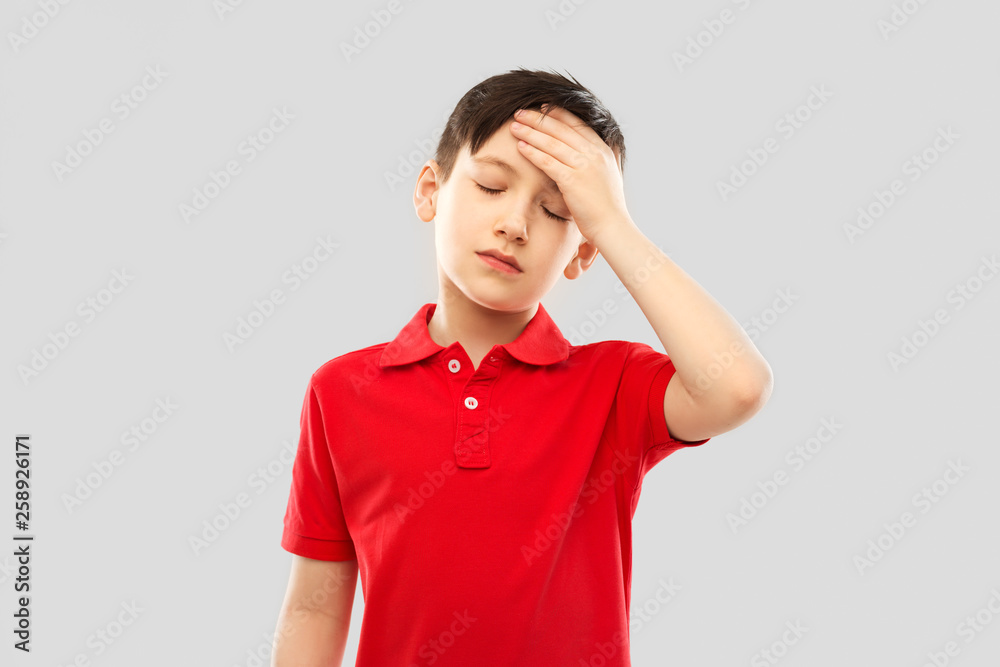 childhood, expressions and people concept - sick little boy in red polo t-shirt suffering from headache over grey background childhood, expressions and people concept - sick little boy in red polo t-shirt suffering from headache over grey background