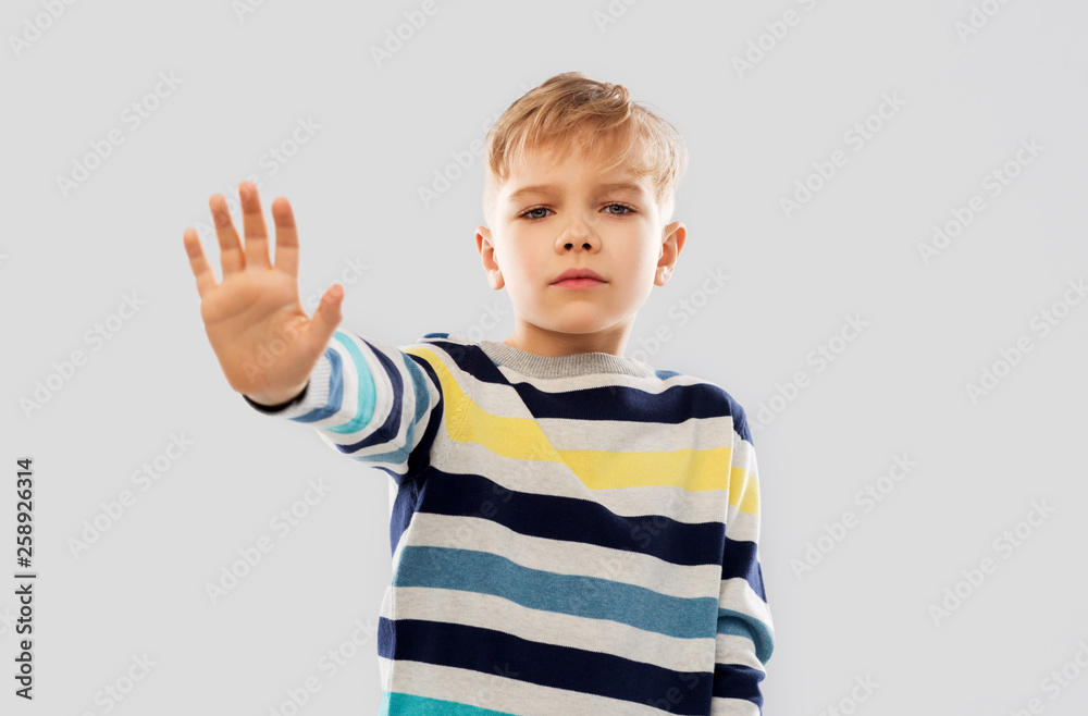 restriction, prohibition and children concept - little boy in striped pullover making stopping gesture over grey background restriction, prohibition and children concept - little boy in striped pullover making stopping gesture over grey background