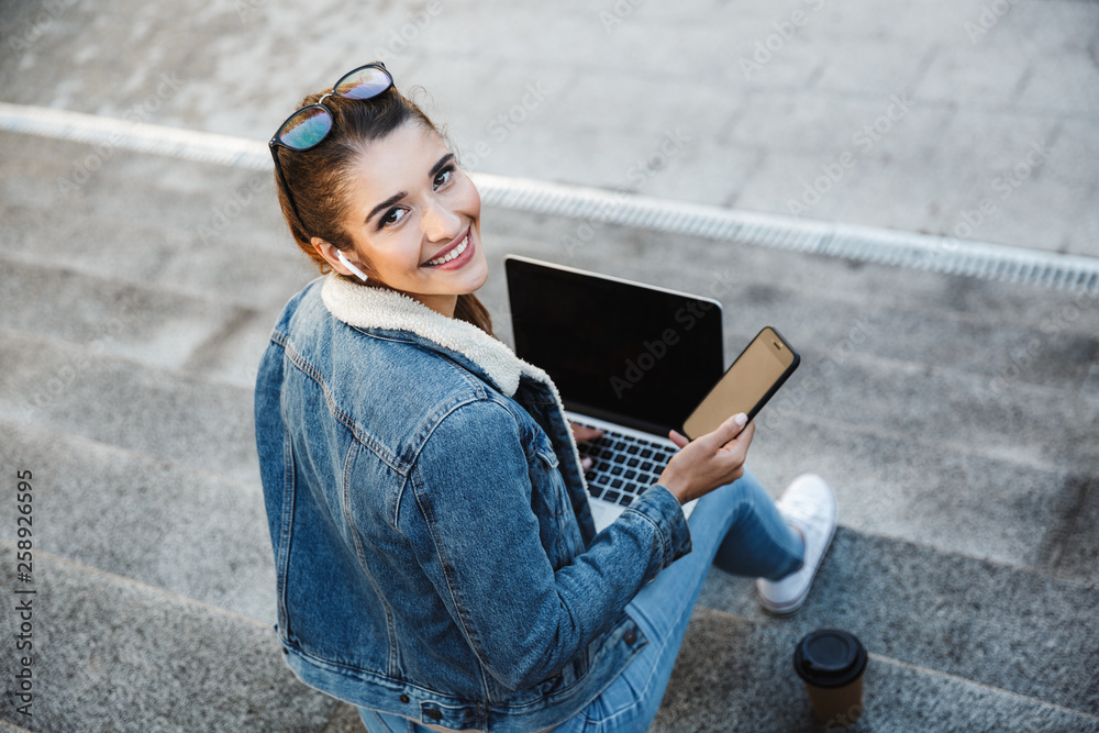 Fototapeta premium Smiling young woman wearing jacket sitting on a bench