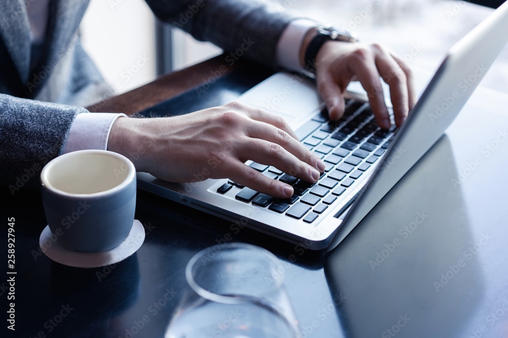 Young man working on his laptop in a coffee shop, rear view of business man hands busy using laptop at office desk. Young man working on his laptop in a coffee shop, rear view of business man hands busy using laptop at office desk.