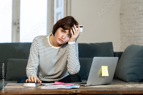 Stressed and overwhelmed young woman paying credit card debts and bills on laptop