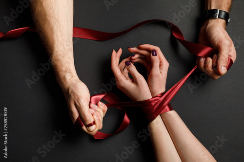 cropped view of man tying red satin ribbon on female hands on black background photo