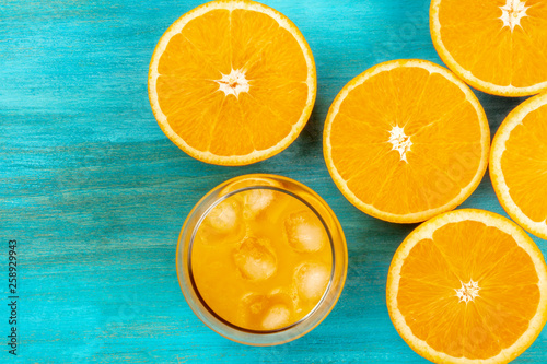 A photo of a glass of fresh orange juice with orange halves, shot from above on a vibrant blue background with a place for text