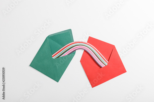 top view of green and red envelopes with multicolored rainbow on grey background