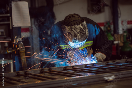 Worker grinding on a metal gate, at his workshop, wearing safety helmet