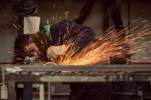 Worker grinding on a metal gate, at his workshop, wearing safety glasses