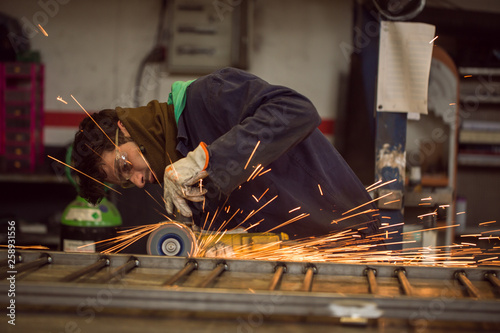 Worker grinding on a metal gate, at his workshop, wearing safety glasses