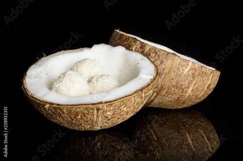 Group of two halves of fresh bio coconut with three small cocoa balls isolated on black glass