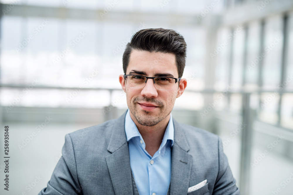 A front view of portrait of young businessman indoors in an office. A front view of portrait of young businessman indoors in an office.