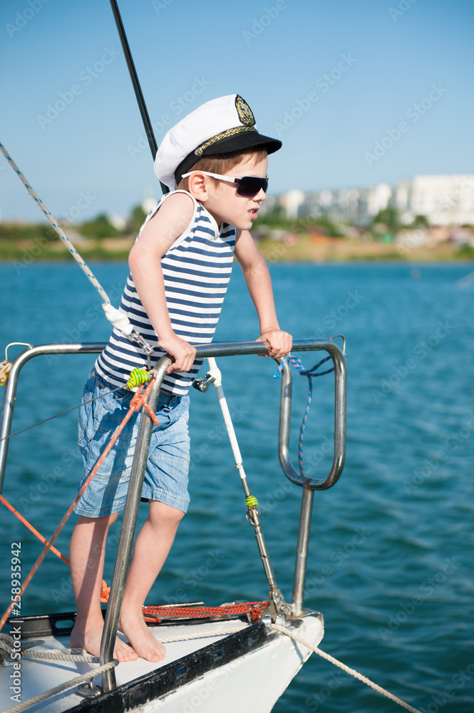 cute little caucasian boy in sunglasses and captain cap on white yacht board cute little caucasian boy in sunglasses and captain cap on white yacht board