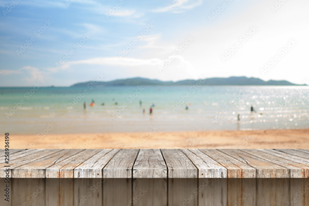 Wood floor against blurry scenic of summer sand beach and cloudy blue sky with copy space
