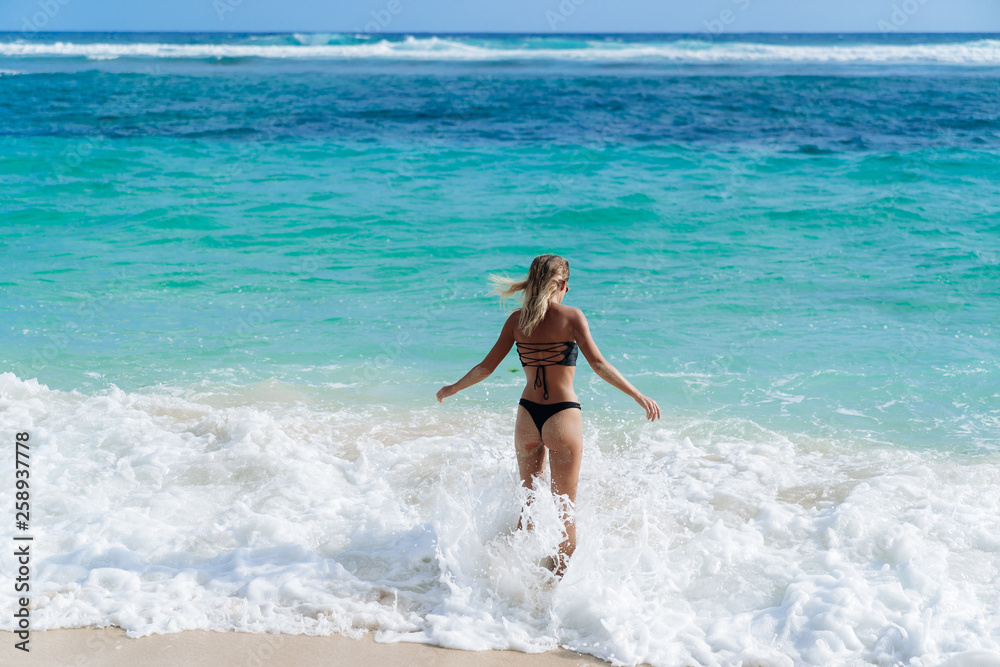 Slim sexy girl in black swimsuit goes swimming in ocean on beach Slim sexy girl in black swimsuit goes swimming in ocean on beach