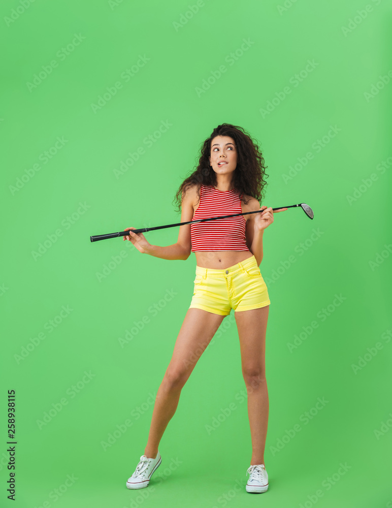 Portrait of delighted woman holding club and playing golf while standing against green wall Portrait of delighted woman holding club and playing golf while standing against green wall