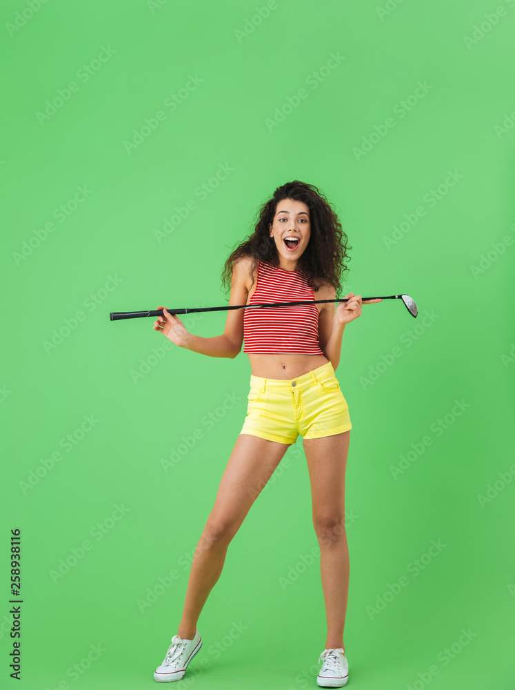 Portrait of energetic woman holding club and playing golf while standing against green wall Portrait of energetic woman holding club and playing golf while standing against green wall