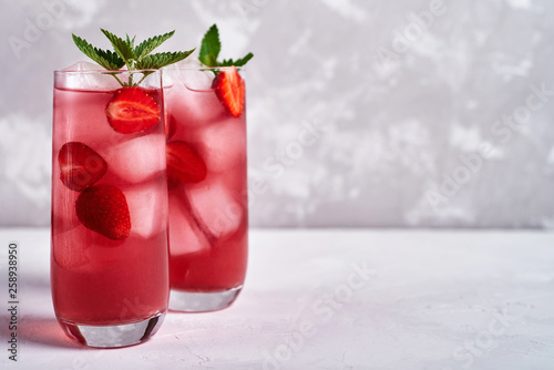 Fresh strawberry lemonade with ice and mint in glass on gray table background, copy space. Cold summer drink. Sparkling glasses with berry cocktail