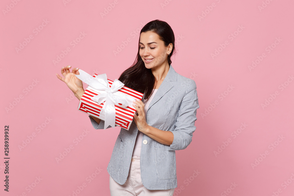 Charming young woman holding red striped present box with gift ribbon isolated on pink pastel background. St. Valentine's Day, International Women's Day, birthday, holiday concept. Mock up copy space. Charming young woman holding red striped present box with gift ribbon isolated on pink pastel background. St. Valentine's Day, International Women's Day, birthday, holiday concept. Mock up copy space.