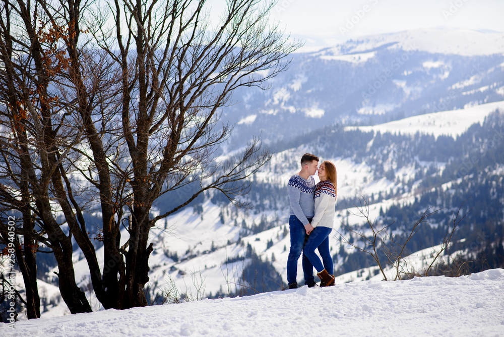 Loving couple playing together in snow outdoor. Winter holidays in mountains. Man and woman wearing knitted clothing having fun on weekends.