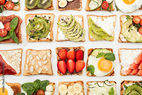 Top view of toasts with cut fruits, vegetables and peanuts on white