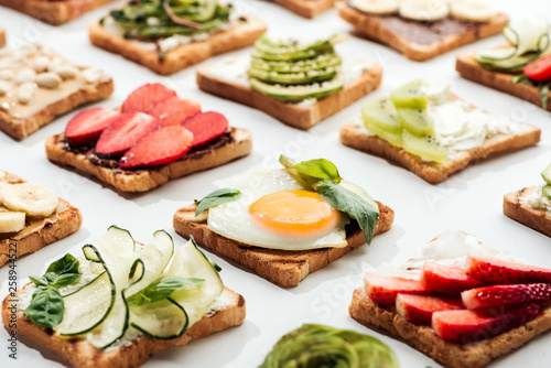 Toasts with cut fruits, fried egg and peanuts on white