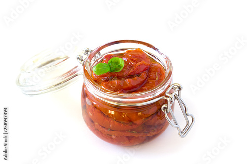 Sun-dried tomatoes in olive oil a glass jar with basil on a gray background  isolated on white background