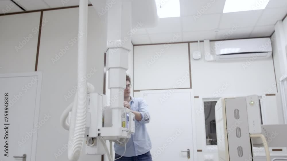 Male intern control and do preparation of roentgen machine before the next radiography examining. Man checking the medicine x-ray equipment for diagnostic procedure in hospital room at internship Male intern control and do preparation of roentgen machine before the next radiography examining. Man checking the medicine x-ray equipment for diagnostic procedure in hospital room at internship