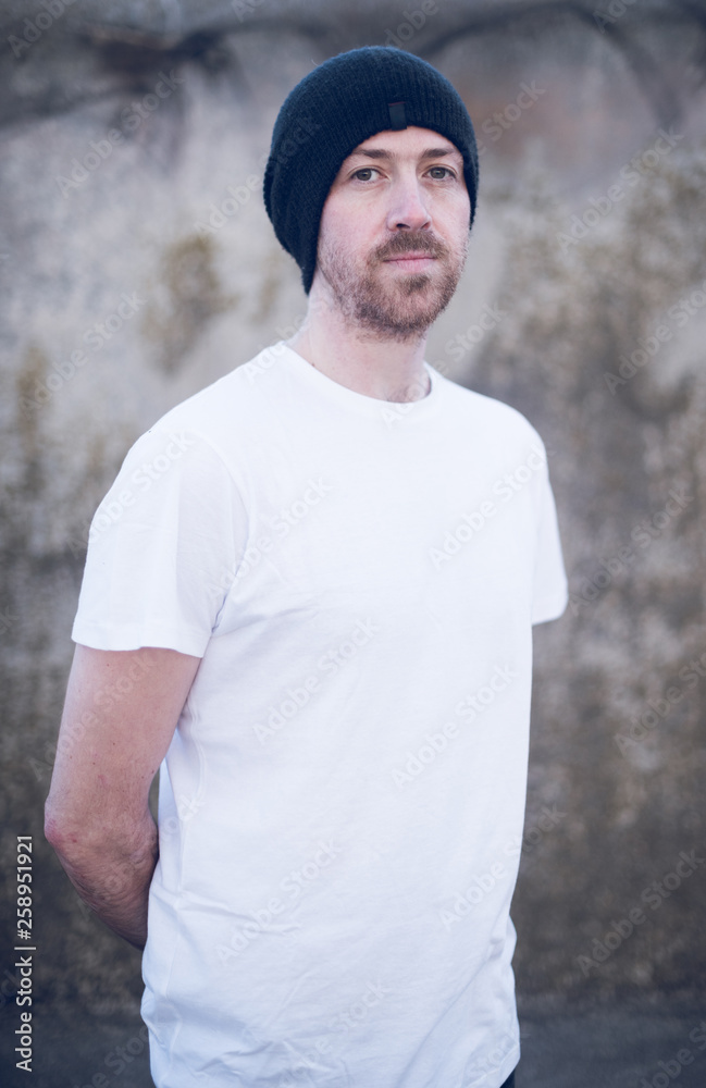 A portrait of young handsome man with stubble and a beanie hat standing alone and contemplating life by the quiet sea, surrounded by raw concrete sea defence wall. A portrait of young handsome man with stubble and a beanie hat standing alone and contemplating life by the quiet sea, surrounded by raw concrete sea defence wall.