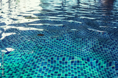 A close up of a clean swimming pool water at the light-blue tiled floor background. One swimming pool drain under rippling indoor pool water. A shallow swimming pool with beautiful water blinks photo