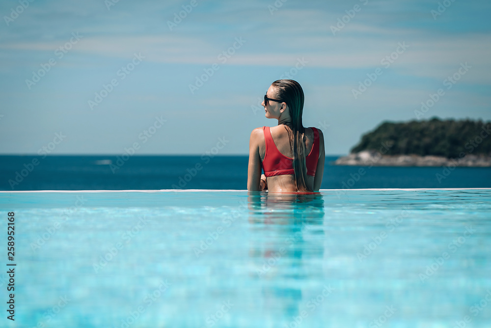 Young woman relaxaing in the swimming pool looking at the ocean view in background l. Beautiful seascape. Trip to warm destination. Phuket. Thailand. Young woman relaxaing in the swimming pool looking at the ocean view in background l. Beautiful seascape. Trip to warm destination. Phuket. Thailand.